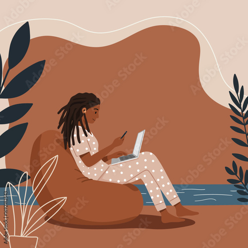Young woman in pajamas comfortably working from home on a laptop and smartphone, embodying remote work and a relaxed digital lifestyle.