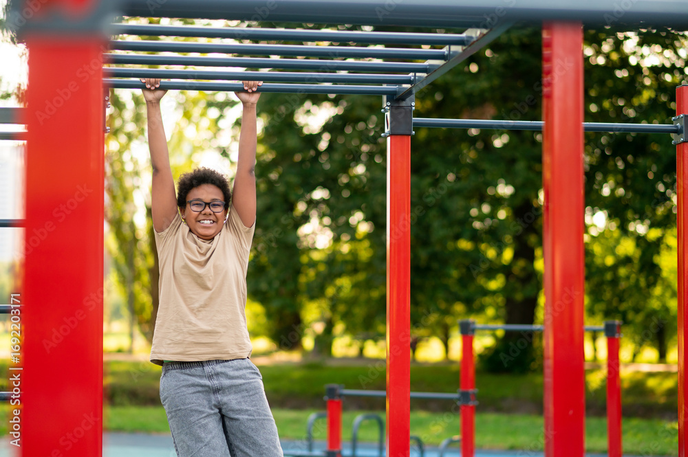 Obraz premium Curly-haired boy doing exercises at the playground in the morning