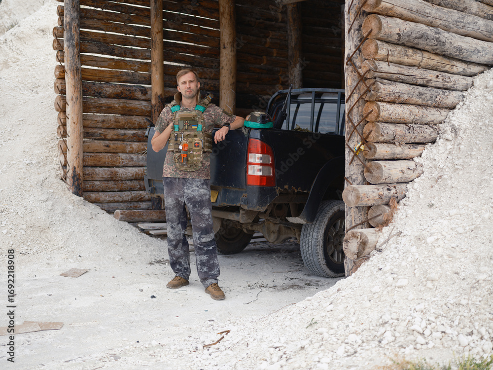 Fototapeta premium Ukrainian soldier standing near a dugout with car.