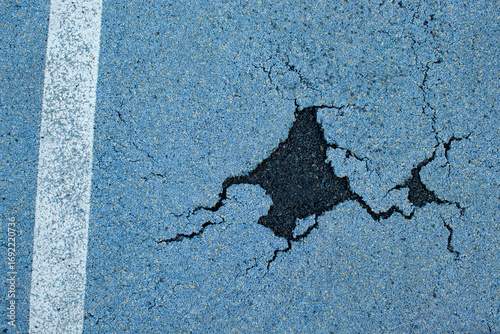 Closeup of damaged blue rubber running track showing a large crack and worn surface. Useful for maintenance, repair, safety hazard, infrastructure, urban sport background and texture themes.