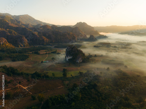 Aerial view of the sun's golden light kissing misty valleys and jagged peaks, a serene landscape unfolds in nature's embrace, Phu Langka Forest Park, Pha Chang Noi, Thailand.