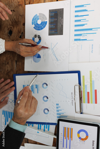 Business team analyzing marketing data and financial reports, pointing at charts and pie graphs with pens during a collaborative corporate meeting in a modern office setting