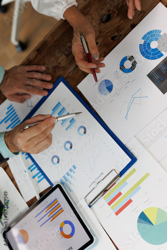 Business colleagues collaborating on a project, analyzing financial charts and graphs on paper and a tablet, using pens to highlight key data during a meeting
