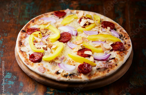 Pizza with chorizo ​​sausage, mozzarella cheese and yellow pepper. Rustic wooden background. Soft focus.