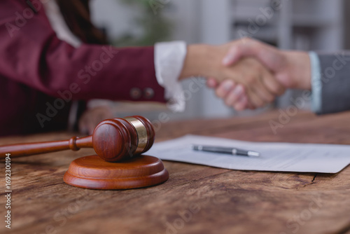 Two lawyers are shaking hands after signing a contract on a wooden table, with a gavel and a pen in the foreground, symbolizing legal agreement and justice