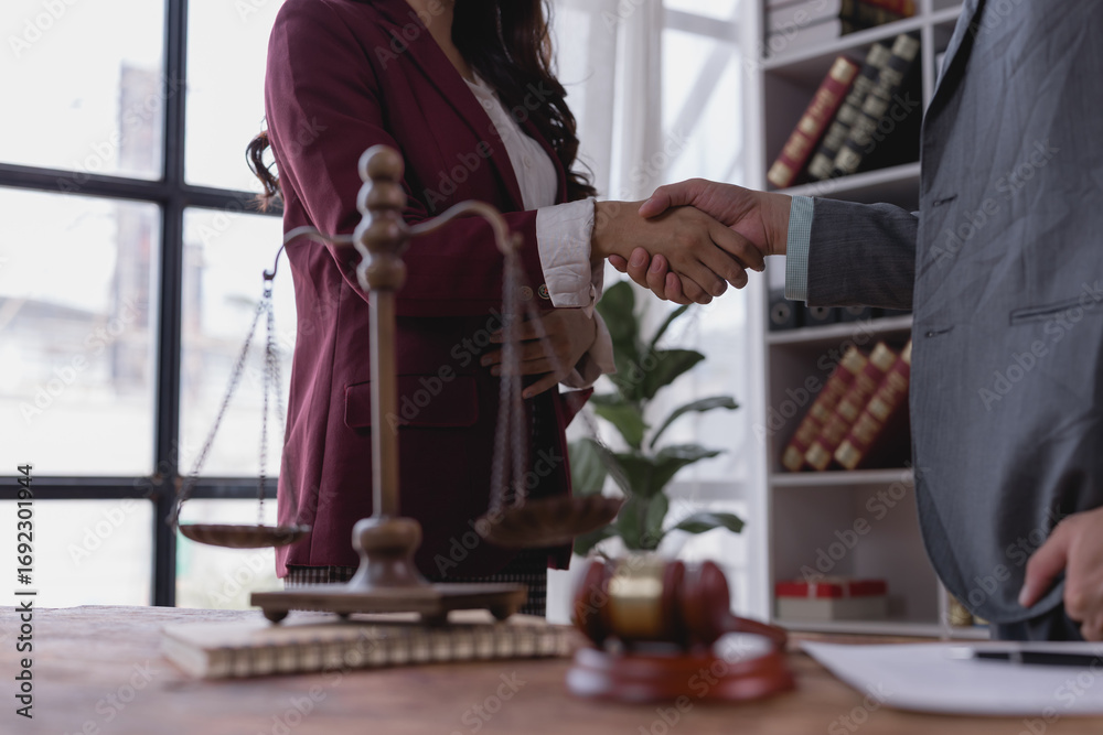 Obraz premium Two lawyers shaking hands in their office after reaching an agreement, with scales of justice and gavel on the table, symbolizing fairness, equality, and the legal process