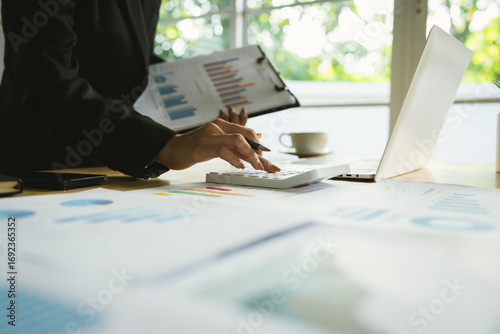 A businessman sits indoors at his office desk analyzing financial graphs on a laptop, planning investments, managing budget, taxes, and savings.