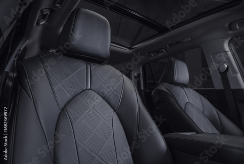 SUV interior with rows of leather seats at night. Front row of car seats in focus and dark interior in the background.