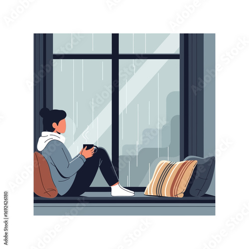 Person sitting by window holding mug with pillows nearby.