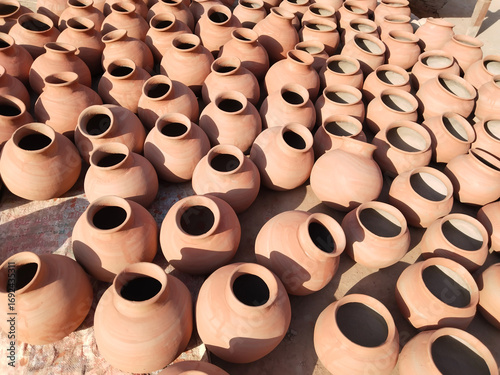 Freshly fired clay pots hand-painted with saffron color and sun-dried in open space for final setting, traditional Indian earthenware pottery placed for curing and long-term storage in sunlight.
