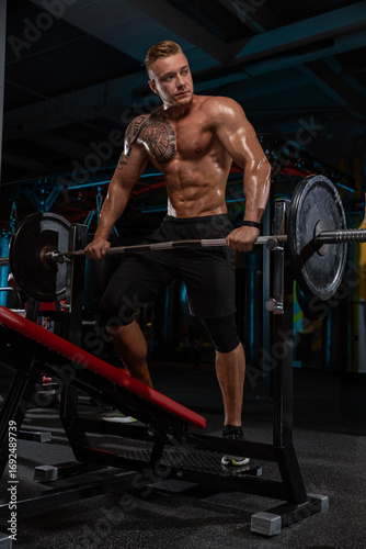 fit man with a strong physique is performing a weightlifting exercise in a gym. Sweat glistens on his skin as he engages in an intense workout surrounded by gym equipment.