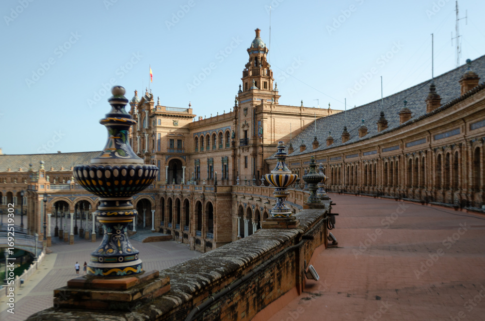 Obraz premium A high-angle shot captures the stunning architecture of the Plaza de España in Seville, Spain. The focus is on the ornate ceramic balustrade in the foreground, leading the eye towards the building