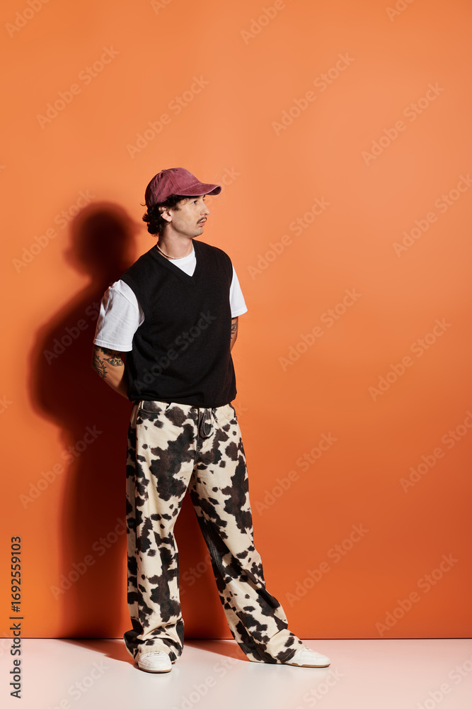 Fototapeta premium Stylish young man exuding confidence in a unique outfit against vibrant orange backdrop