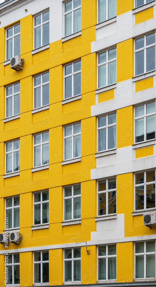 Fototapeta premium Yellow and white building facade with windows and air conditioners