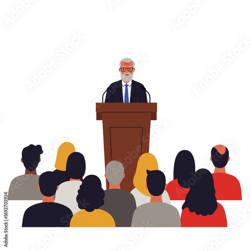 A man with a beard and glasses gives a speech from a podium to an audience.