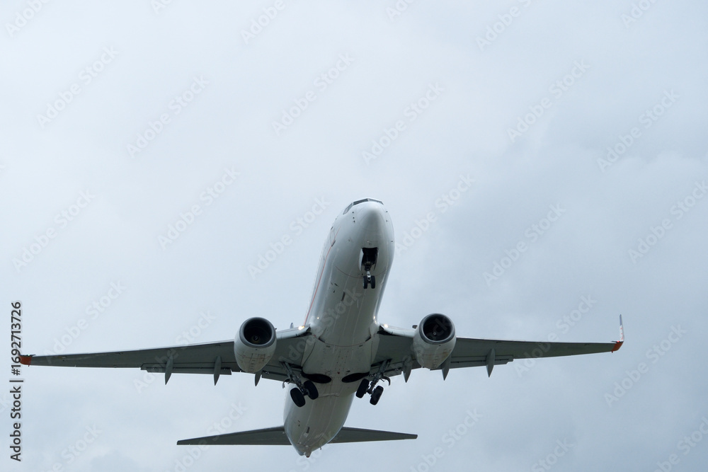Fototapeta premium An airplane flies through clouds, observed from the runway.