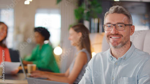 Portrait Of Mature Businessman Working On Laptop In Informal Seating Area Of Modern Office