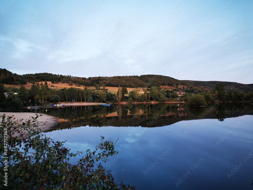 Fototapeta premium Ruhige Abendstimmung am Edersee im September, mit sanften Hügeln, spiegelglattem Wasser und Blick auf den Campingplatz. Naturidylle und friedvolle Atmosphäre. Copyright Sarah Bömer. 