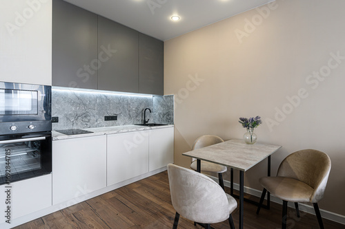 Modern kitchen with gray cabinets, white lower cabinets, marble backsplash, and a small dining area with a table and three chairs
