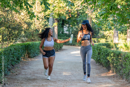 Two latin women running and drinking water in a park