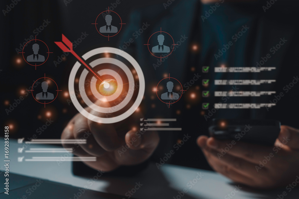 Fototapeta premium Businessman using a smartphone to target customers and achieve business goals, completing a checklist while focusing on marketing and CRM strategies in a dynamic office setting