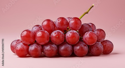 Bunch of ripe red grapes resting on a pink surface, showcasing their freshness and vibrant color, creating a simple yet appealing still life composition.