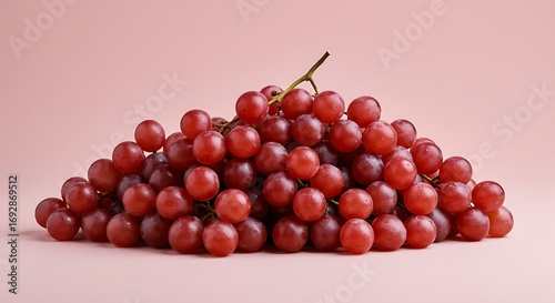 Pile of fresh red grapes resting on a light pink surface, showcasing their vibrant color and appealing texture in a simple still life composition.