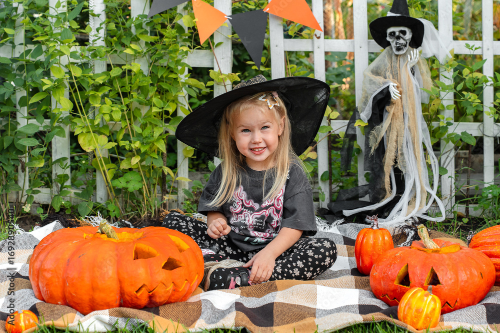 Fototapeta premium Little girl is getting ready for Halloween, decorating the garden with pumpkins and a skeleton