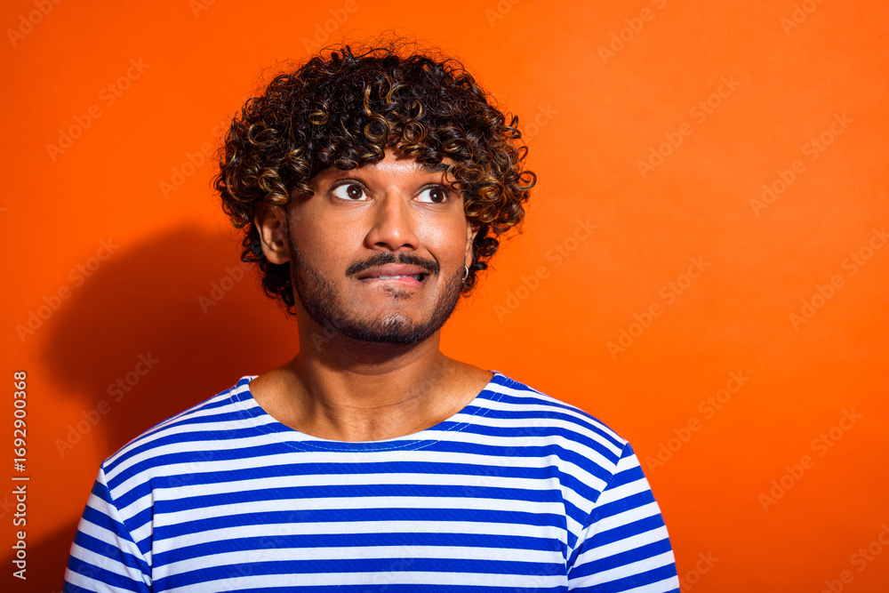 Fototapeta premium Portrait of a young man with curly hair wearing a striped shirt in front of a vibrant orange background