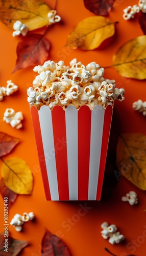 Popcorn in a Striped Box Surrounded by Colorful Autumn Leaves on a Vibrant Or...
