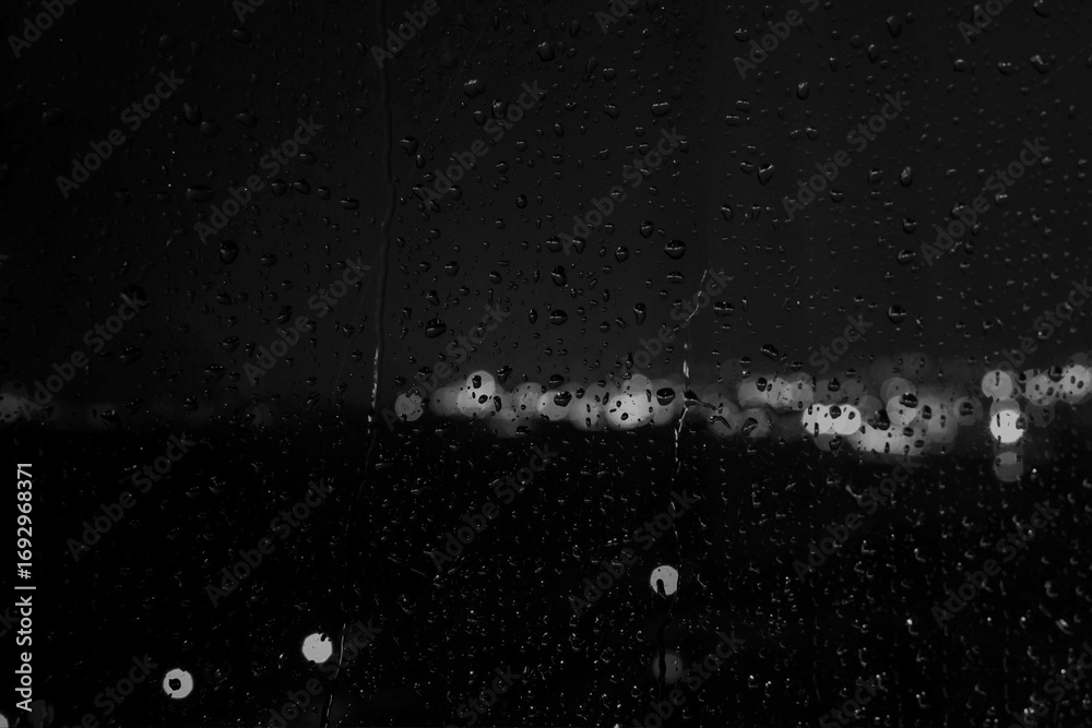 Fototapeta premium Black and white photo of rain drops on a glass window creating abstract texture and moody atmosphere.