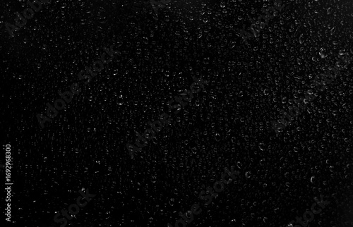 Black and white photo of rain drops on a glass window creating abstract texture and moody atmosphere.