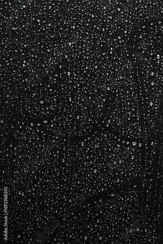 Black and white photo of rain drops on a glass window creating abstract texture and moody atmosphere.