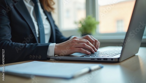 Businesswoman typing on laptop at desk with paperwork and plant  