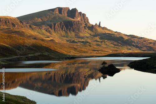 Peaceful morning view of Loch Fada reflecting the dramatic rock formations of the Old Man of Storr on the Isle of Skye, bathed in soft golden light