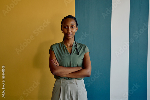 Portrait of African young businesswoman standing arms crossed against colorful wall in office