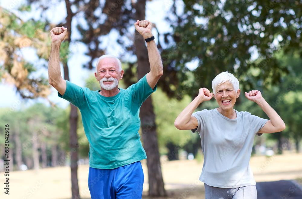 Obraz premium Smiling active senior couple jogging exercising and having fun and giving high five together celebrating victory in the park