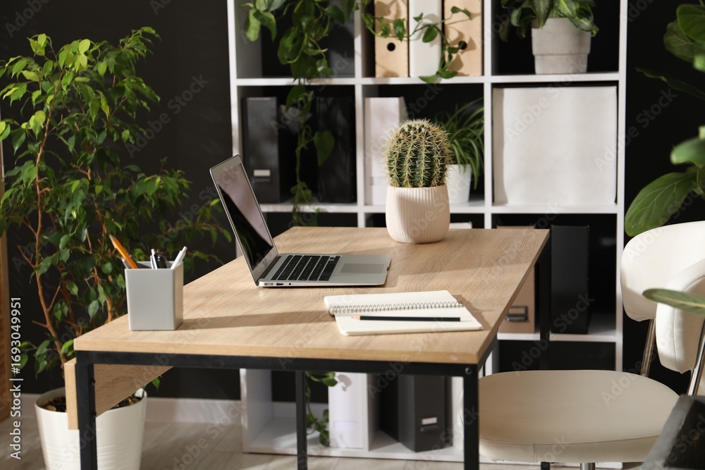 Fototapeta premium Stylish workplace with laptop, stationery and floral decor in office. Biophilic interior design