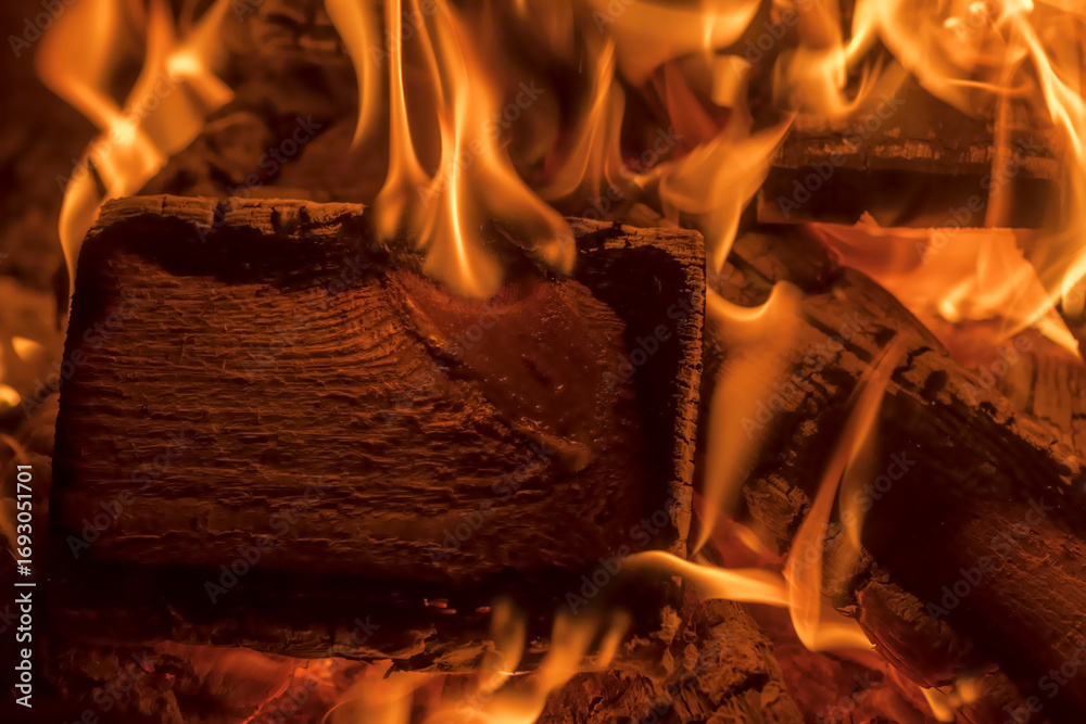 Fototapeta premium Sosnowe polana płoną jasnymi, pomarańczowymi płomieniami, eksponując swoją fakturę powierzchni podczas palenia w ognisku. Ogień emanuje ciepłą poświatą z widocznymi językami wijącymi się i tańczącymi