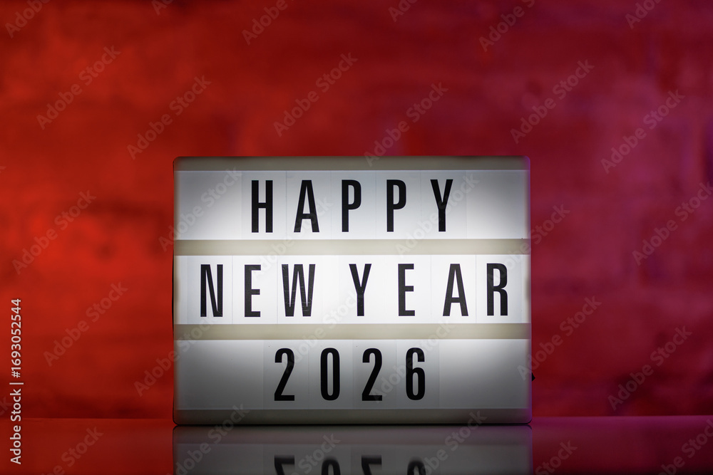 Obraz premium A cinematic lightbox with the words Happy New Year 2026 illuminated, placed against a rustic brick background on a glossy white reflective table
