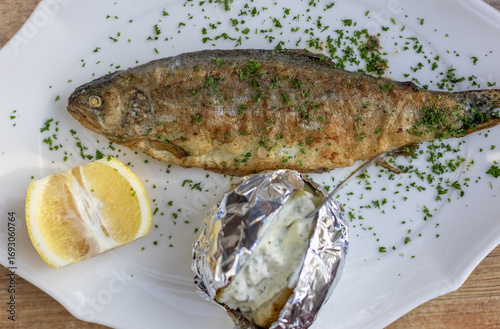 golden fried trout with tangy lemon and creamy baked potato on white plate.