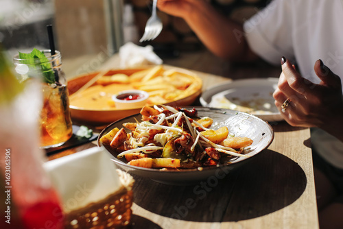 Plate with fries and vegetables served on wooden table in restaurant. Closeup of fresh food with sauce and drink. Tasty dinner detail. Casual dining lifestyle concept.