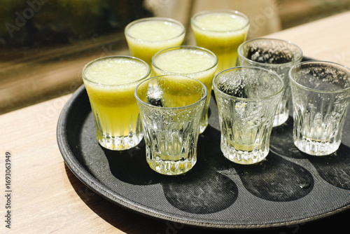 Tray with glasses of shots on wooden table. Green drinks with foam closeup. Party celebration alcohol detail. Bar lifestyle concept.