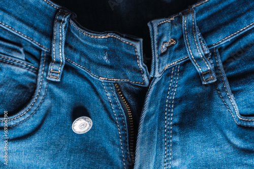 Close-up of blue denim jeans with pocket textures and seam details and broken buttons visible.