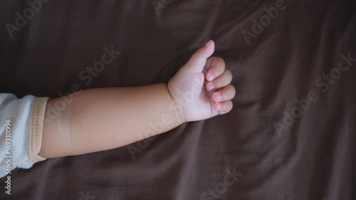 Adorable baby's tiny hand and arm giving a gentle thumbs-up on soft brown fabric
