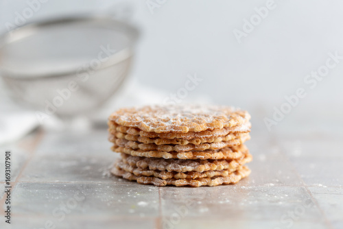 Pizzelles sprinkled with Powdered Sugar stacked on a white tile kitchen counter