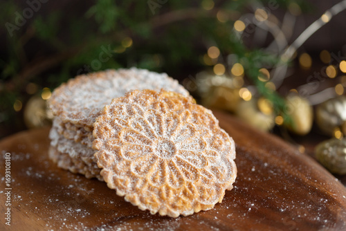 Pizzelles Sprinkled with Powdered Sugar on a Wood Tray with Christmas Decor in Background