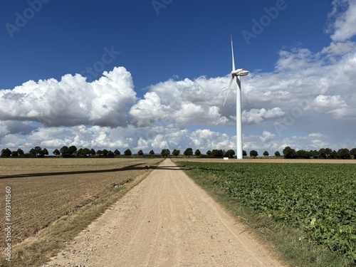 Wind turbine with cloudy sky in a field along the road and trees in the background in 52399 Golzheim, NRW, Germany