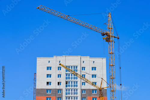 Tower crane in action to build multi-storey residential building against blue sky