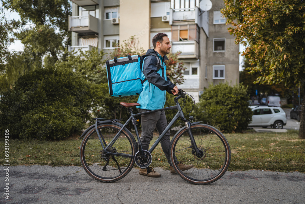 Obraz premium Delivery man riding bicycle smiling carrying insulated backpack in city park